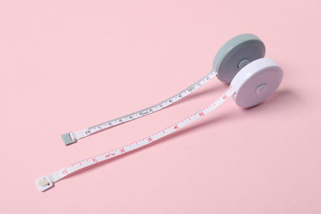 Measuring tapes on pink background, closeup view