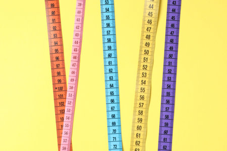 Different measuring tapes on yellow background, flat lay