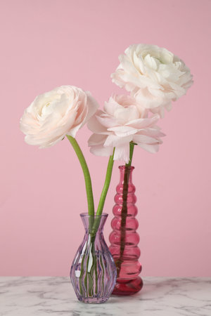 Beautiful flowers in vases on white marble table against pink background, closeup