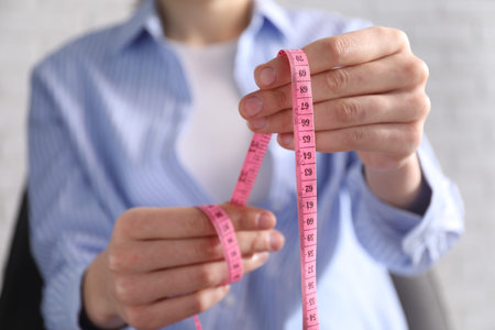 Woman with measuring tape on light background, closeup