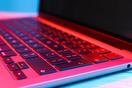 Stylish modern laptop in neon lights on white background, closeup