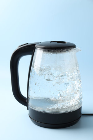 Water boiling in electric kettle on light blue background