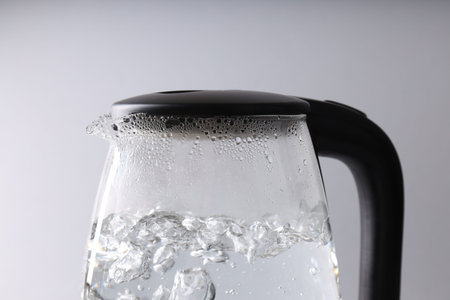 Water boiling in electric kettle on light grey background, closeup