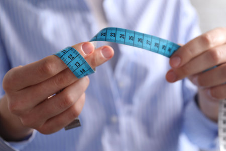 Woman with measuring tape on light background, closeup