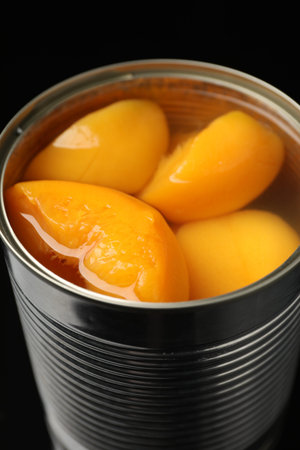 Pickled peaches in tin can on black background, closeup