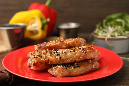 Tasty baked spring rolls with rice paper and sesame seeds served on wooden table, closeup
