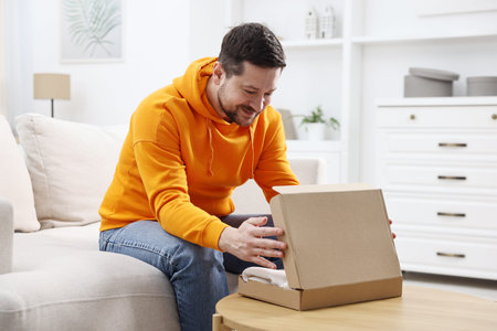 Happy man opening parcel on sofa at table at home