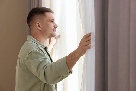 Man opening beautiful window curtains at homeの写真素材