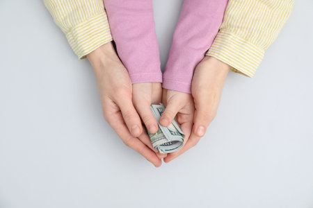 Alimony. Mother and daughter with dollar banknotes on light grey background, top view