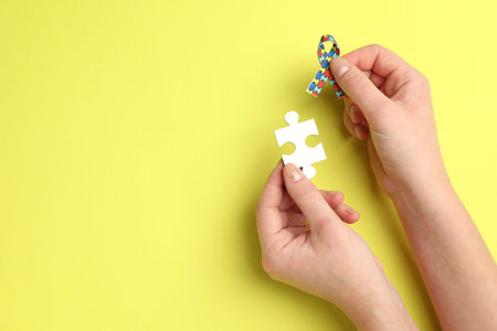 Autism. Woman with puzzle piece and ribbon on yellow background, top view. Space for text