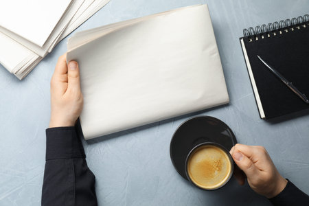 Man with newspaper and coffee at grey table, top view