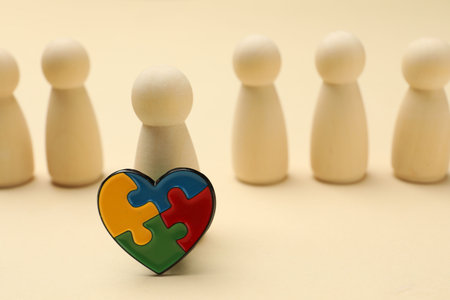 Autism. Human figures and heart made of puzzles on beige background, closeup