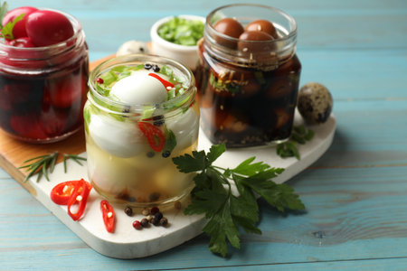 Tasty pickled quail eggs in glass jars and ingredients on light blue wooden table, closeupの写真素材