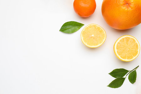 Different fresh citrus fruits and green leaves on white background, flat lay. Space for text