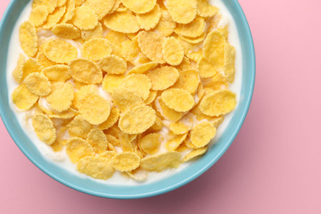 Tasty corn flakes with milk in bowl on pink table, top view