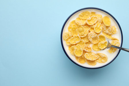 Tasty corn flakes with milk in bowl served on light blue table, top view. Space for text