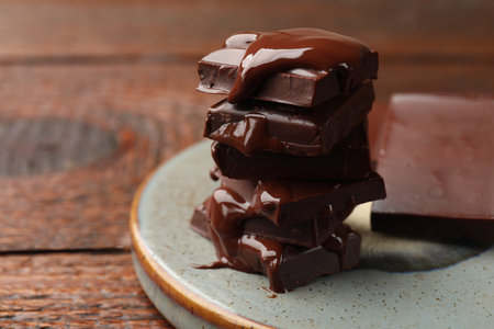 Pieces of chocolate melting on wooden table, closeup