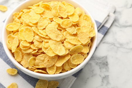 Tasty corn flakes in bowl on white marble table, closeup. Space for text