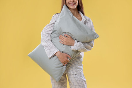 Beautiful woman in stylish pajamas with pillow on yellow background, closeup