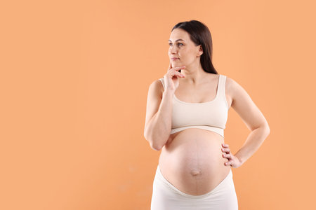 Choosing name for baby. Thoughtful pregnant woman on orange background, space for text