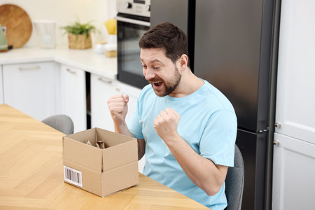 Excited man with open parcel at wooden table at home