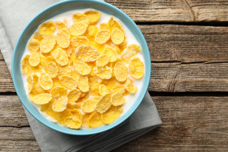 Tasty corn flakes with milk in bowl on wooden table, top view. Space for text