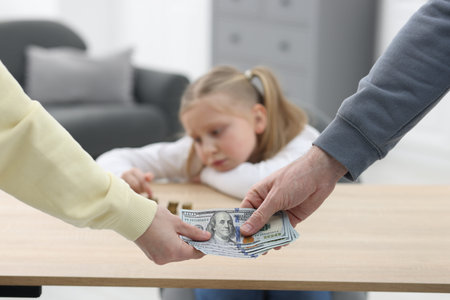 Alimony. Man giving money to ex-wife while his sad daughter counting coins at table indoors,...