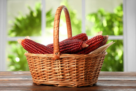 Red corn cobs in basket on wooden table indoors