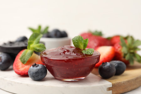 Different sweet jams in glass bowls, strawberries, blueberries and mint on table, closeupの写真素材