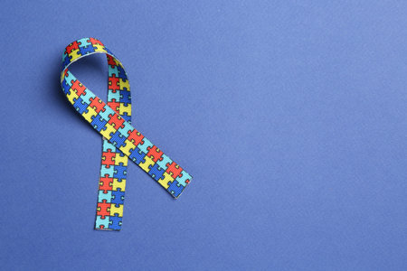 Autism. Colorful puzzle ribbon on blue background, top view. Space for text