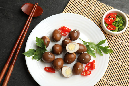 Pickled quail eggs, chopsticks and ingredients on black table, flat lay