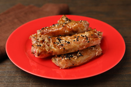 Tasty baked spring rolls with rice paper and sesame seeds served on wooden table, closeup