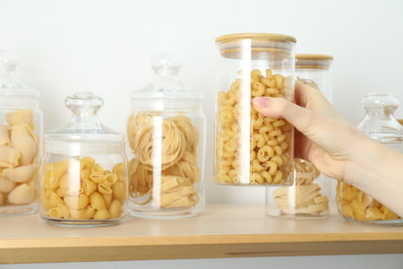 Woman taking jar with pasta from wooden shelf, closeup