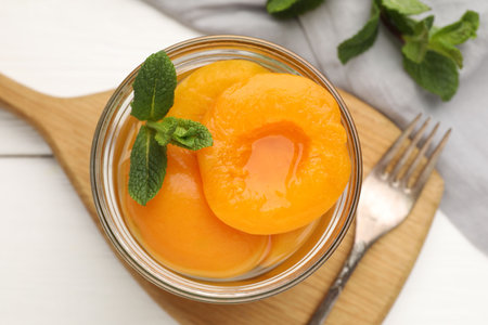 Pickled peaches and mint leaves in glass jar on white wooden table, flat layの写真素材