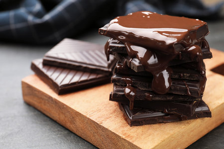 Pieces of chocolate melting on wooden board, closeup