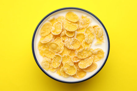 Tasty corn flakes with milk in bowl on yellow table, top view