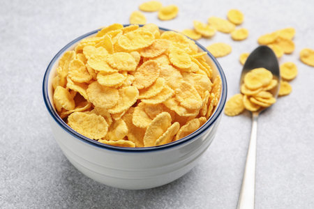 Tasty corn flakes in bowl and spoon on light grey table, closeup