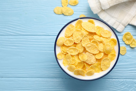 Tasty corn flakes with milk in bowl on light blue wooden table, top view. Space for text