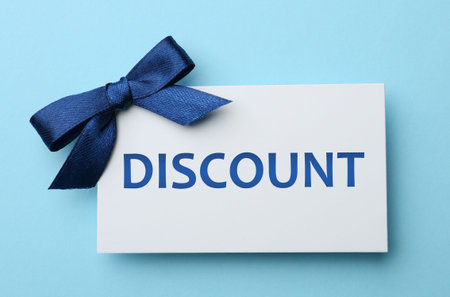 Discount card with bow on light blue background, top view