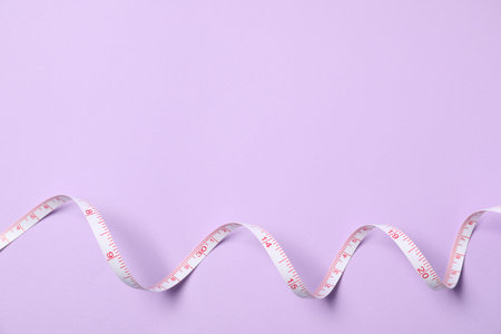 One measuring tape on violet background, top view. Space for text