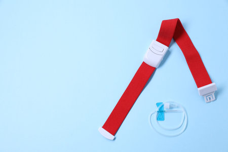 Medical tourniquet and IVF tubing with needle on light blue background, flat lay. Space for textの写真素材