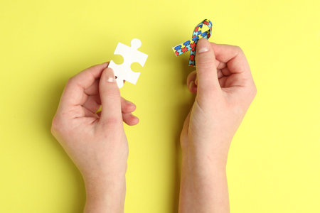 Woman with puzzle piece and ribbon on yellow background, top view