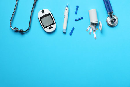 Diabetes. Digital glucometer, test strips, lancets, pen and stethoscope on light blue background, flat lay. Space for textの写真素材