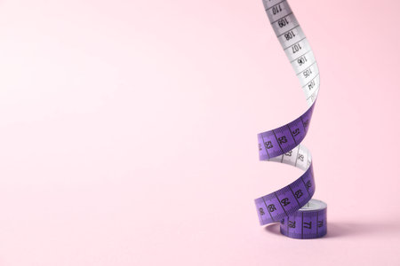 One measuring tape on pink background, closeup. Space for text