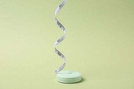 One measuring tape on light green background, closeup