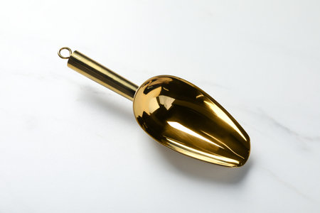 Golden scoop on white marble table, above view