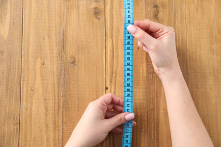 Woman with measuring tape on wooden background, top view. Space for text