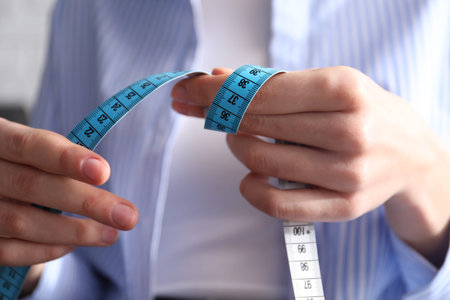 Woman with measuring tape on light background, closeup
