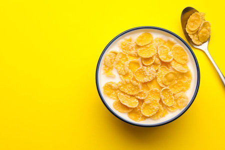 Tasty corn flakes with milk in bowl served on yellow table, flat lay. Space for text