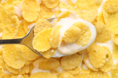 Spoon with tasty corn flakes and milk, top view
